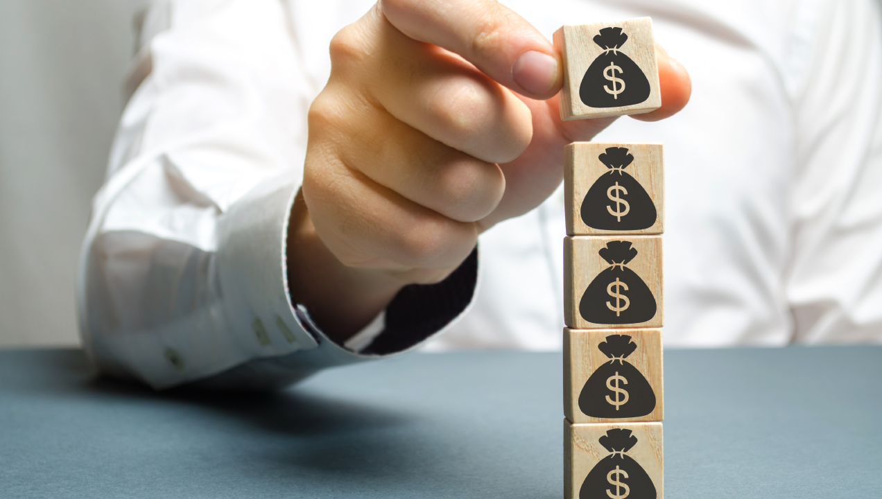 alguém a empilhar cubos de madeira e neles um ícone de saco de dinheiro alguém a empilhar cubos de madeira e neles um ícone de saco de dinheiro