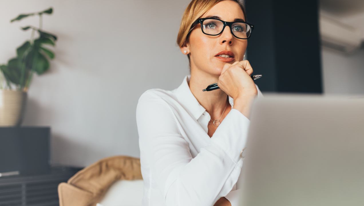 Senhora sentada à secretária de frente para o computador e a pensar