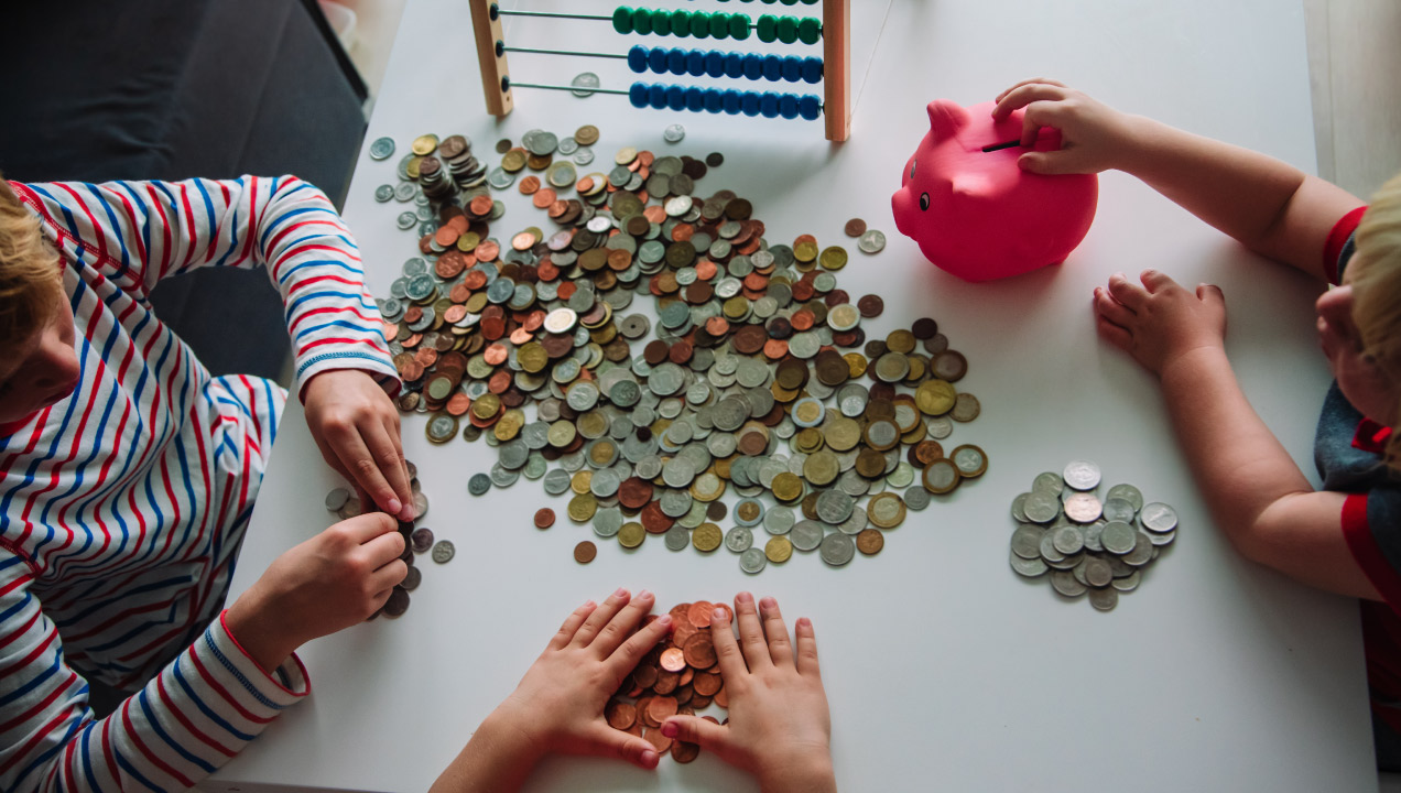 Crianças à volta da mesa contam moedas e colocam no mealheiro