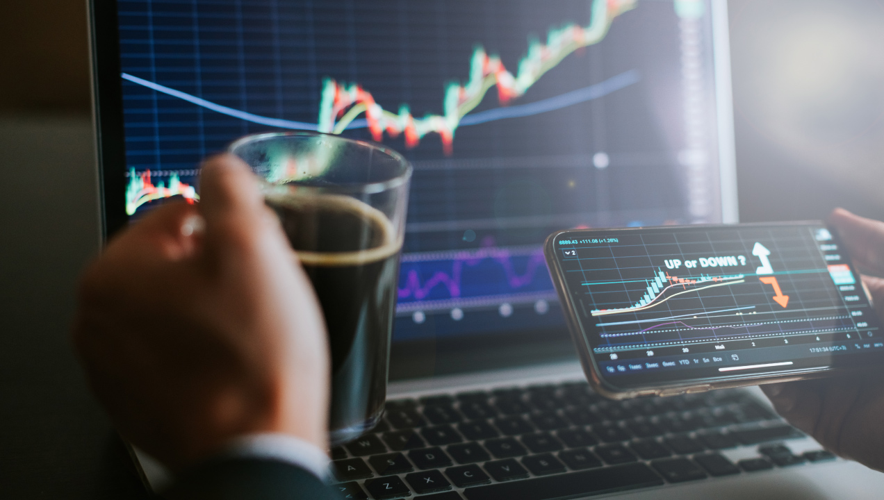 Senhor a segurar uma chávena de café e a ver gráficos de ações