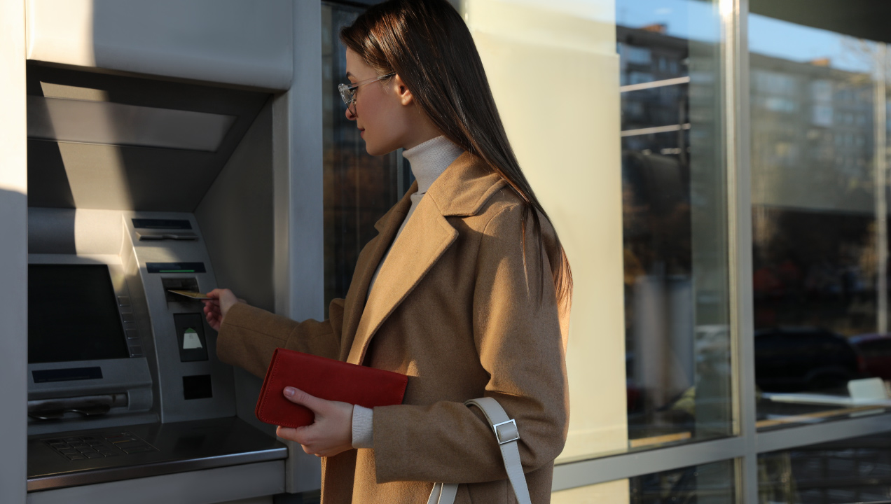 jovem mulher a utilizar um ATM com cartão bancário