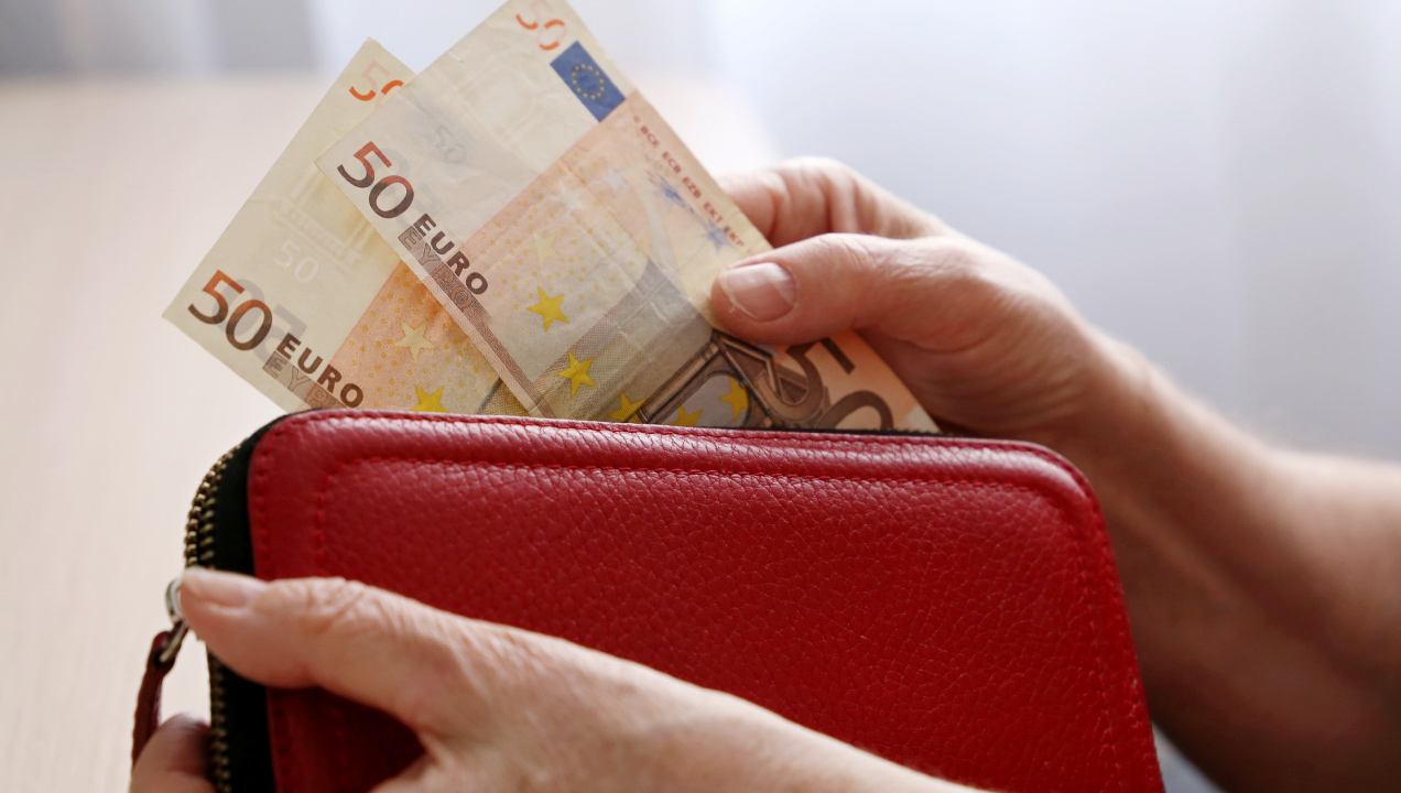 Mãos a segurar uma carteira vemelha e duas notas de 50 euros