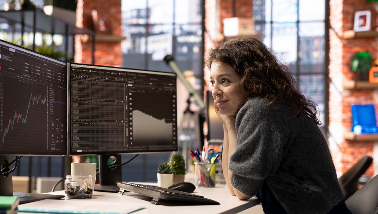 Mulher à secretária do escritório contempla gráficos e outros dados no computador