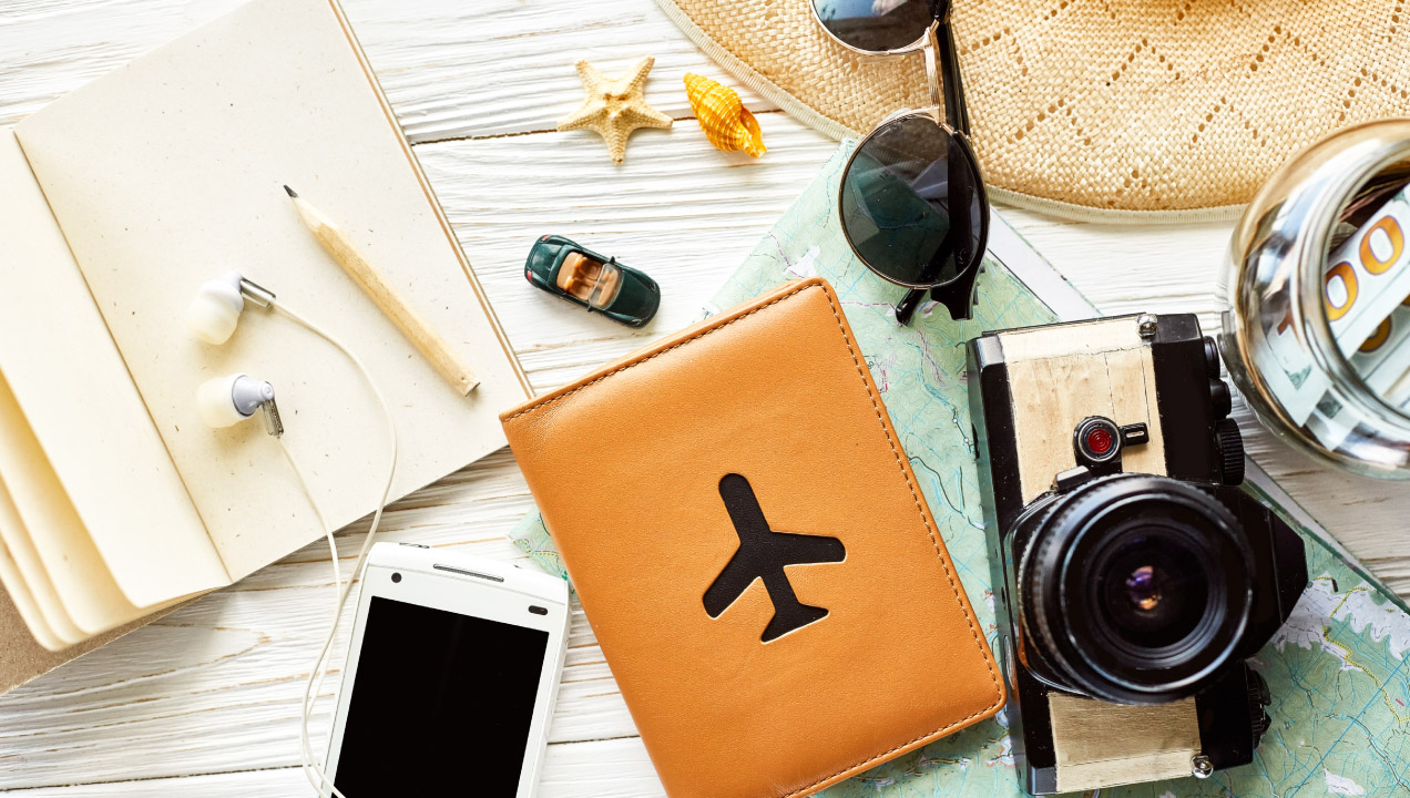 Passaporte, câmara fotográfica, óculos de sol, bloco de notas e chapéu em cima da mesa