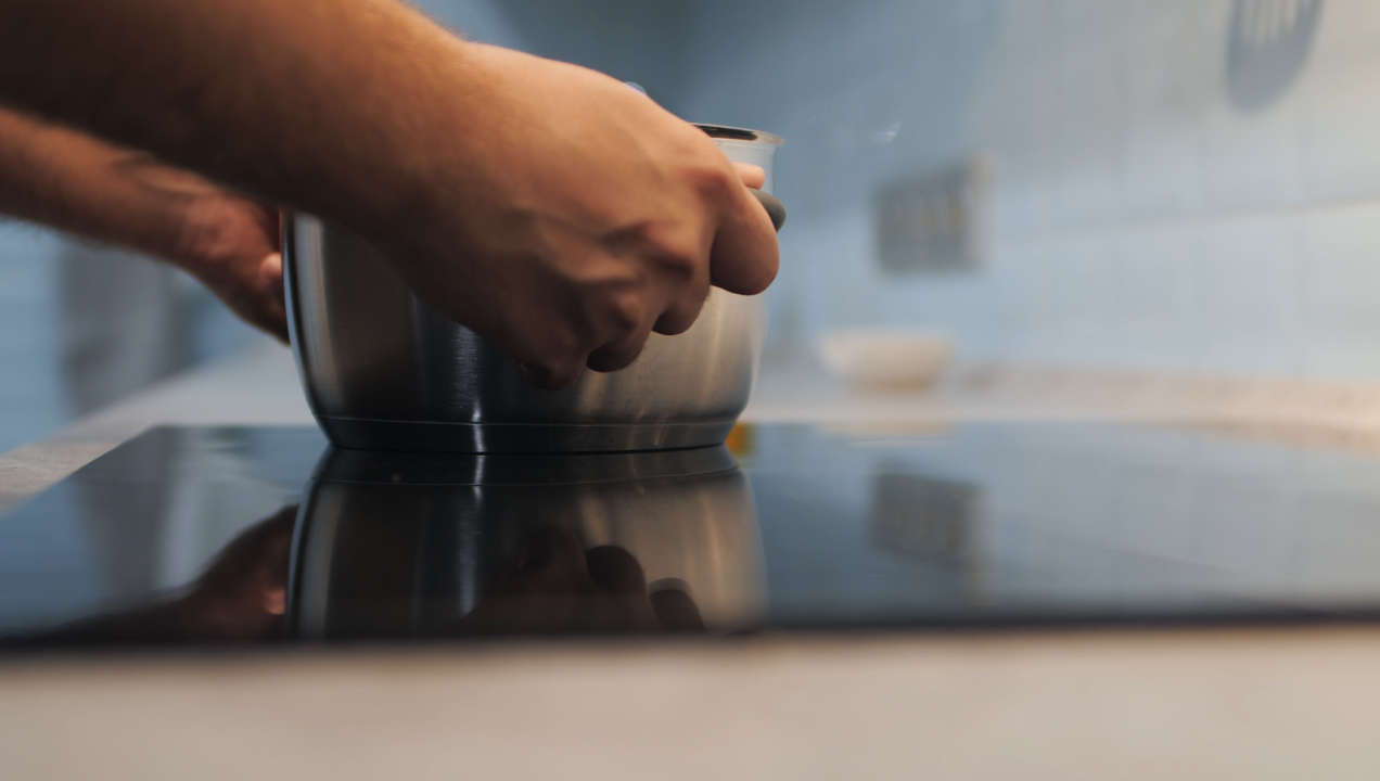 Mãos seguram panela em cima de placa de fogão