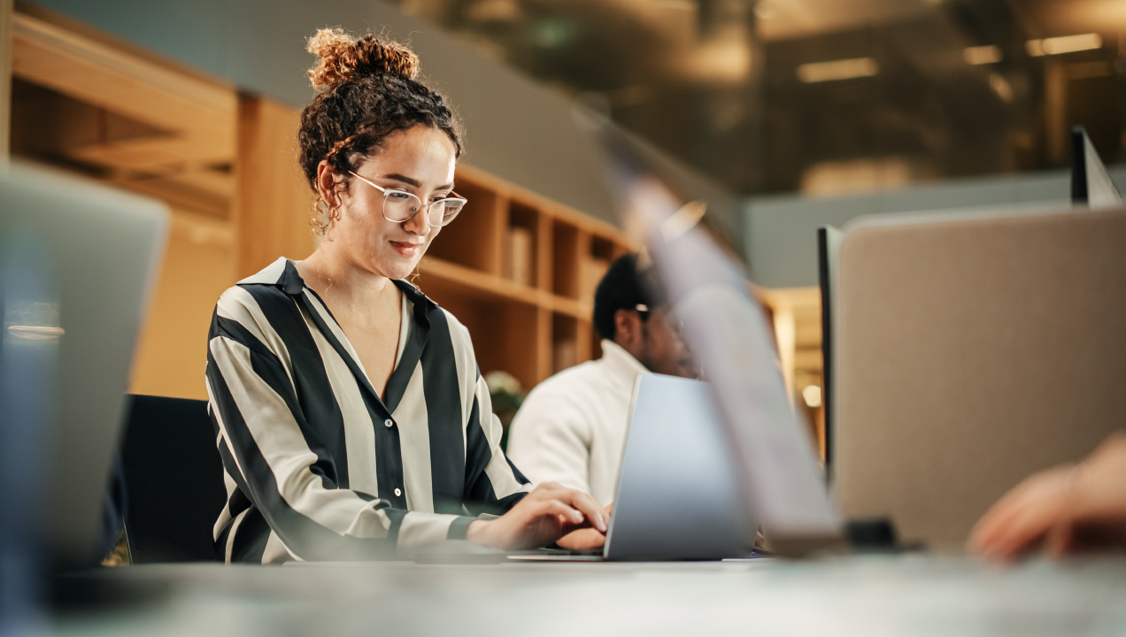 Senhora sentada numa secretária de escritório e mexer no computador num ambiente corporativo