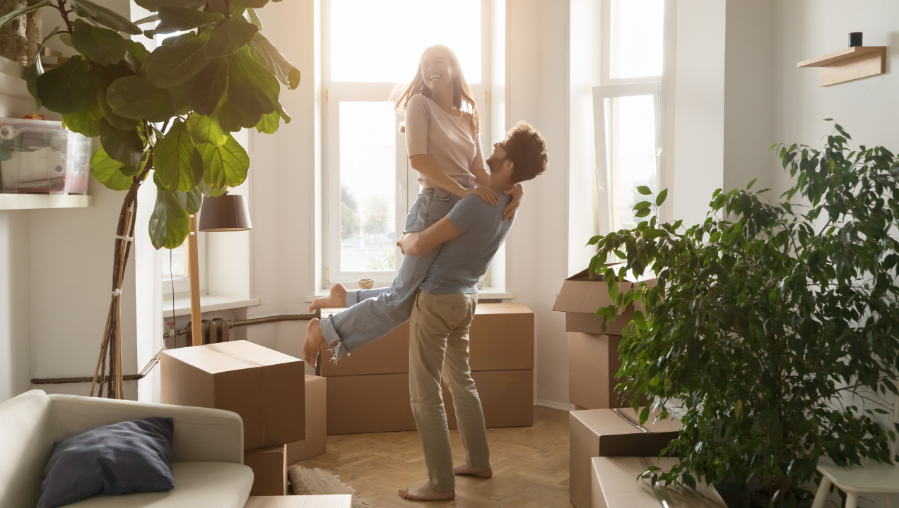 Casal feliz na sala da sua casa e várias caixas de mudanças