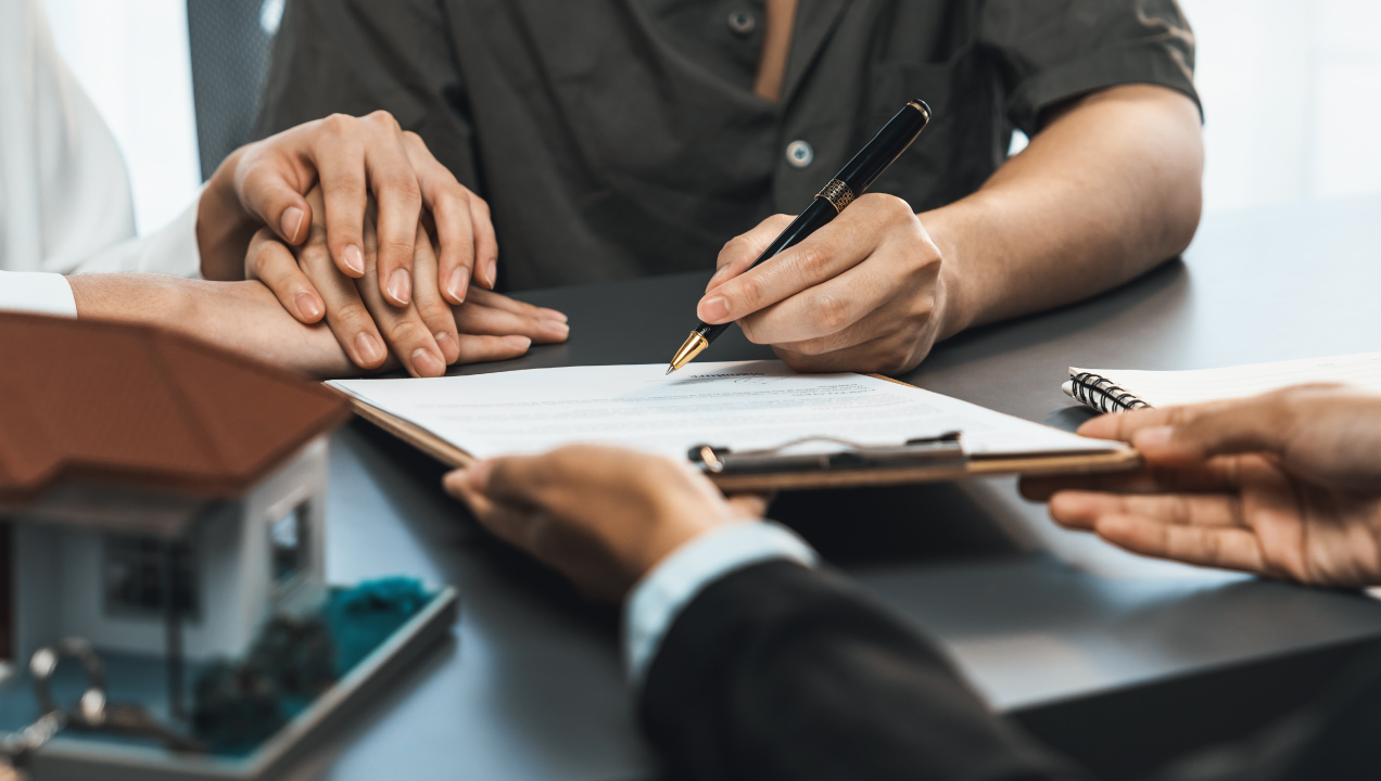 Casal a dar a mão enquanto senhor assina uns documentos 