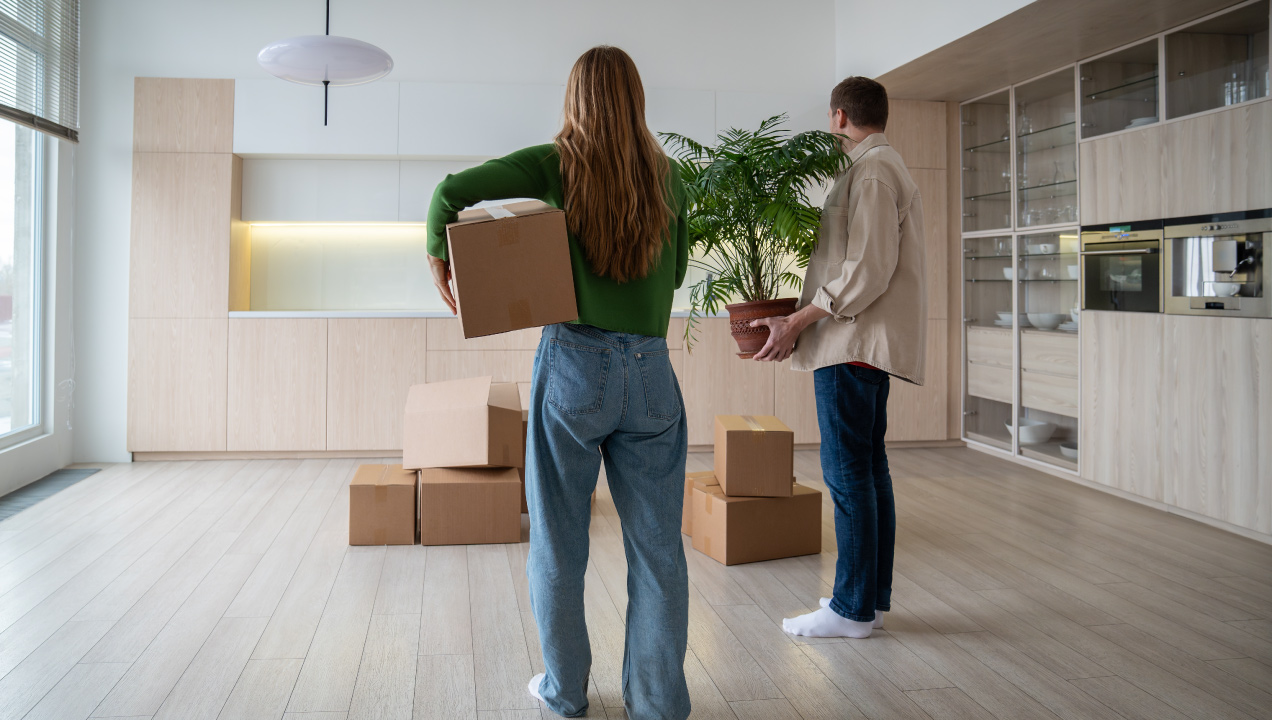Casal numa casa nova com caixas de mudanças e uma planta