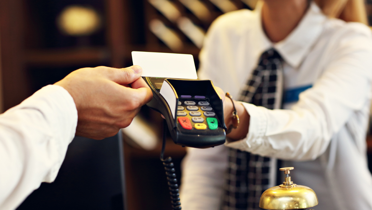 Senhor a passar o cartão contactless num terminal de pagamento segurado por um trabalhador  assegurando uma transação num hotel