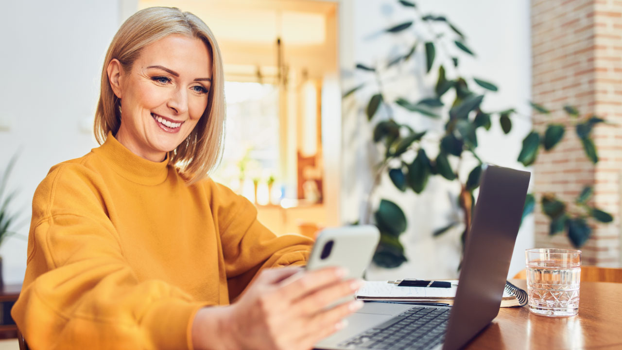 empresária a olhar para o telemóvel e computador portátil