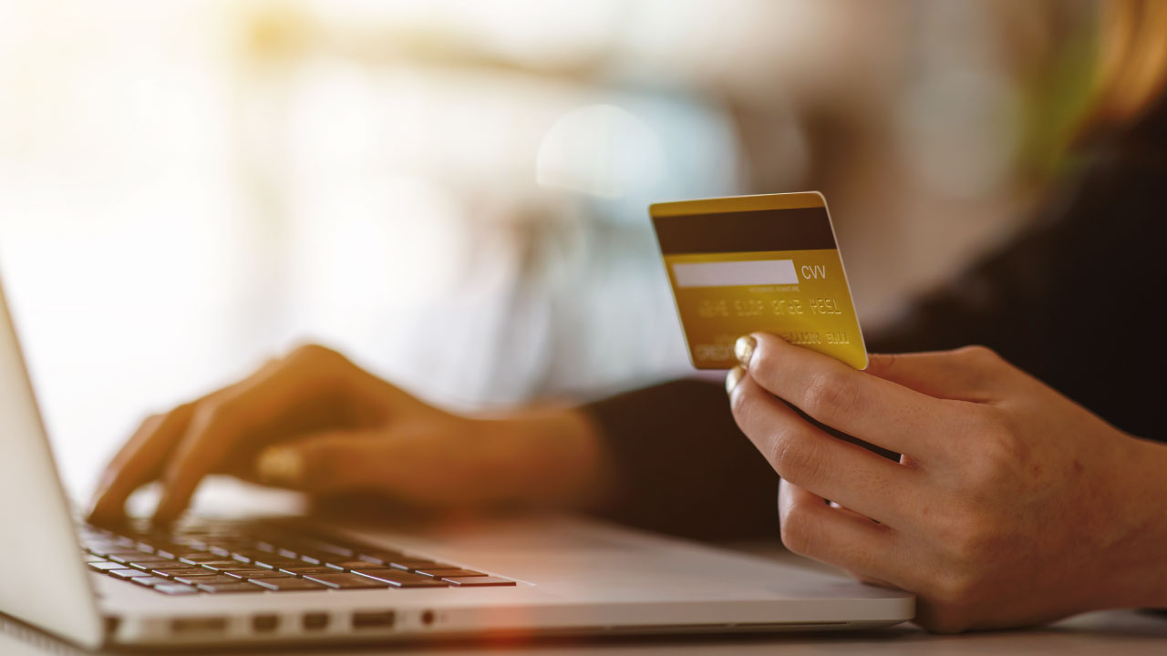pessoa no computador e com um cartão de crédito na mão