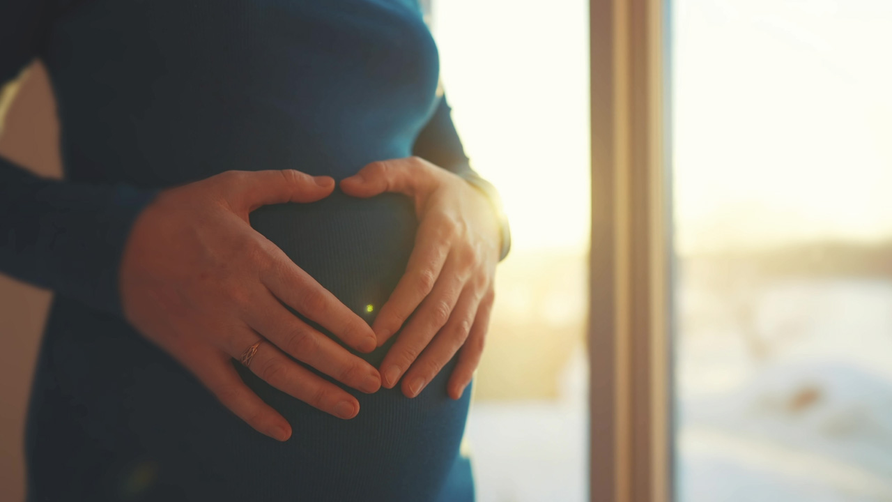 senhora grávida a fazer um coração na barriga com os dedos da mão