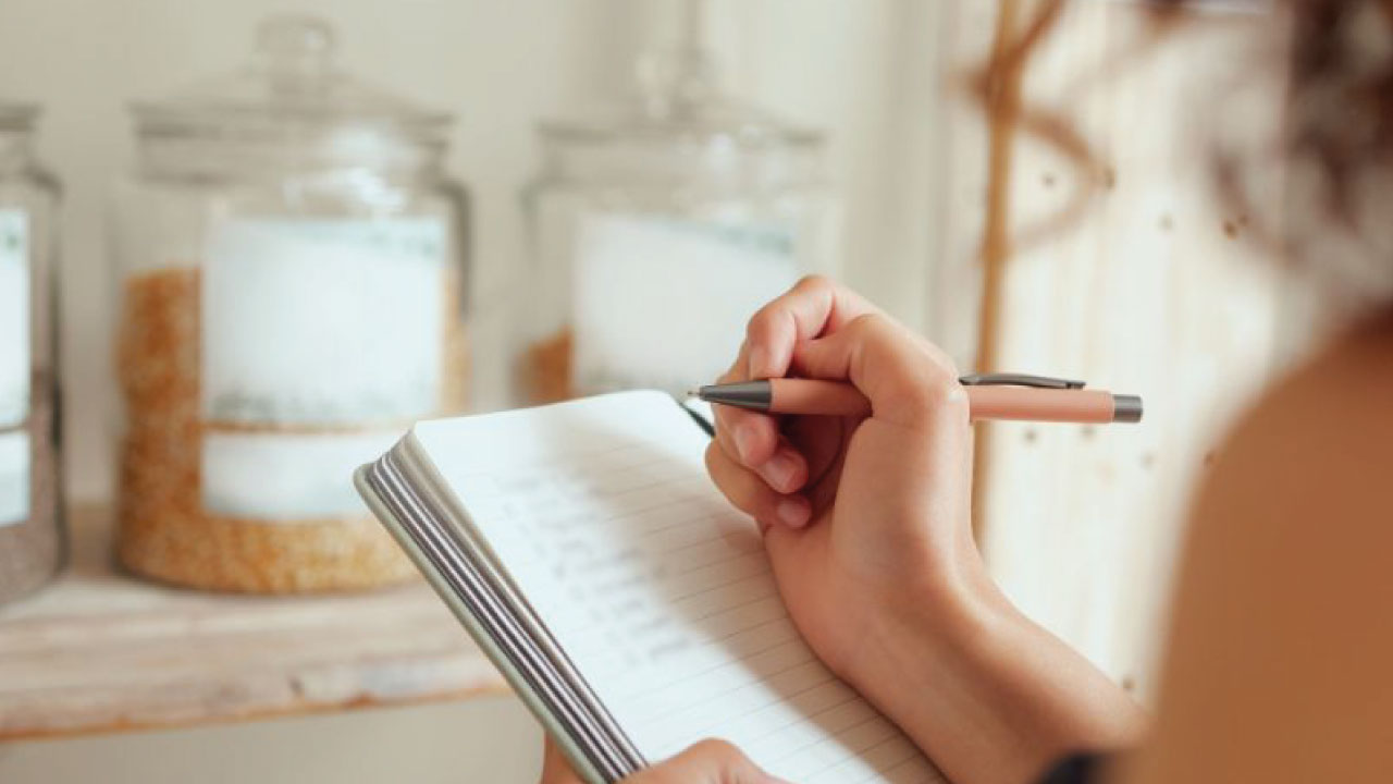 senhora a escrever uma lista de compras num caderno