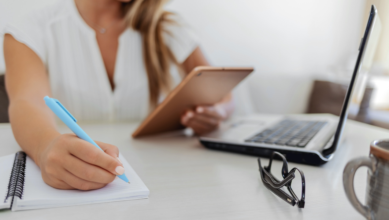 Senhora sentada na secretária a mexer no tablet e a tirar notas