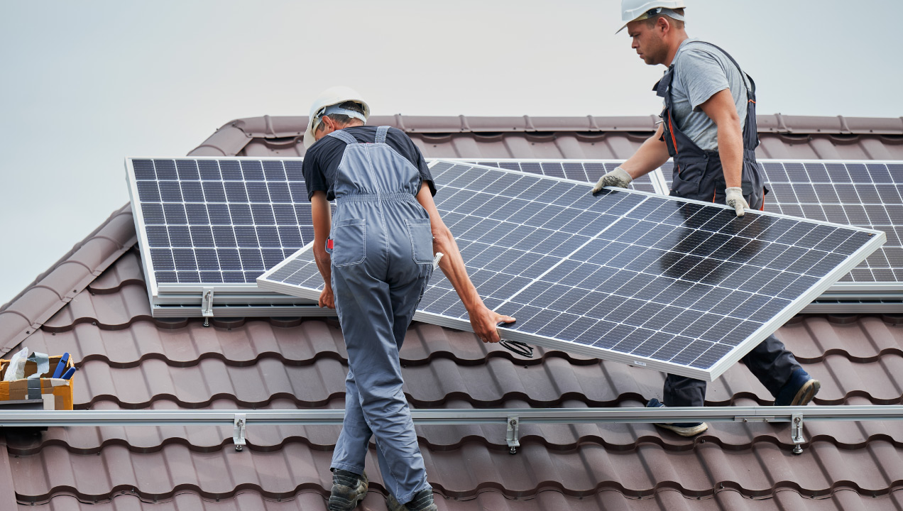 Dois técnicos a instalar painéis solares num telhado