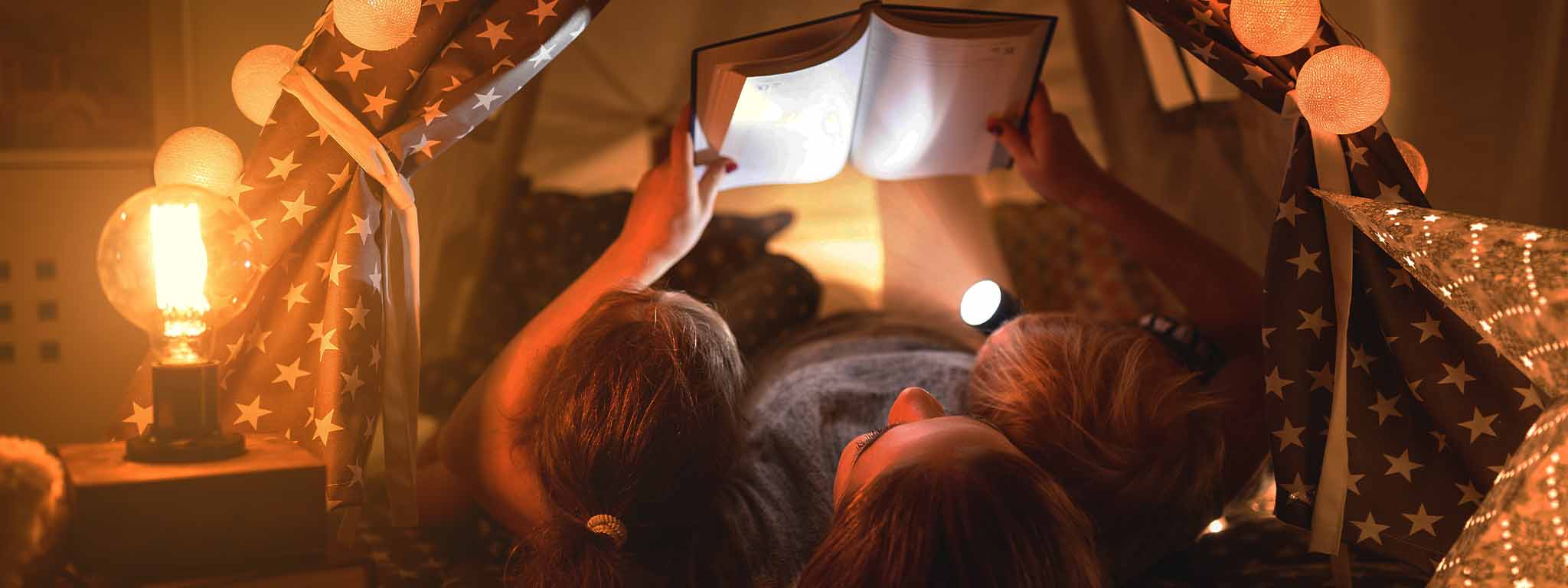 mãe a ler um livro para os seus dois filhos com uma lanterna