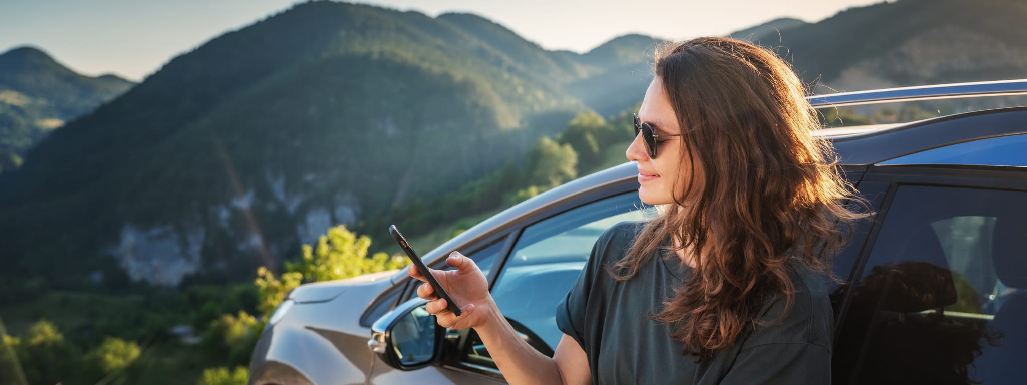 senhora encontada ao carro a olhar para o telemóvel