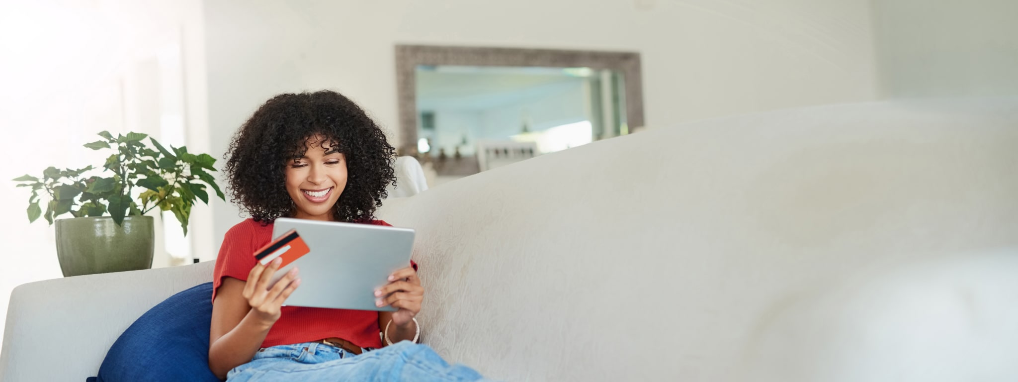 senhora sentada no sofá com tablet na mão e cartão bancário