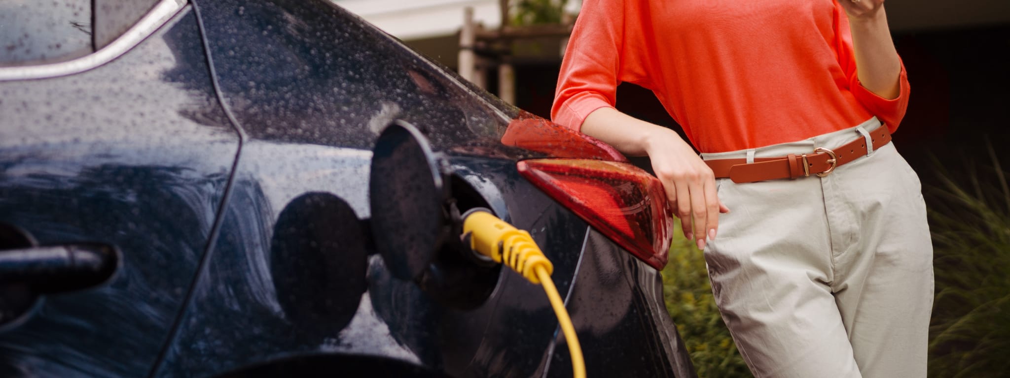 pessoa encostada a um carro elétrico que está a carregar