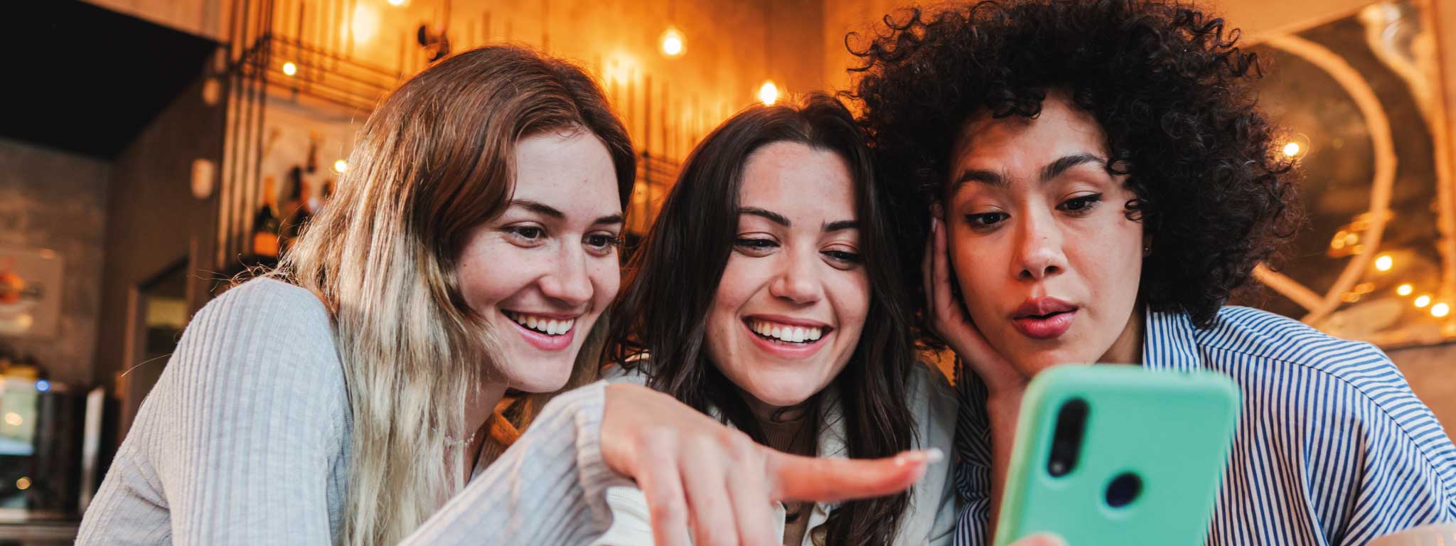 três jovens a olhar para um telemóvel com um ar divertido