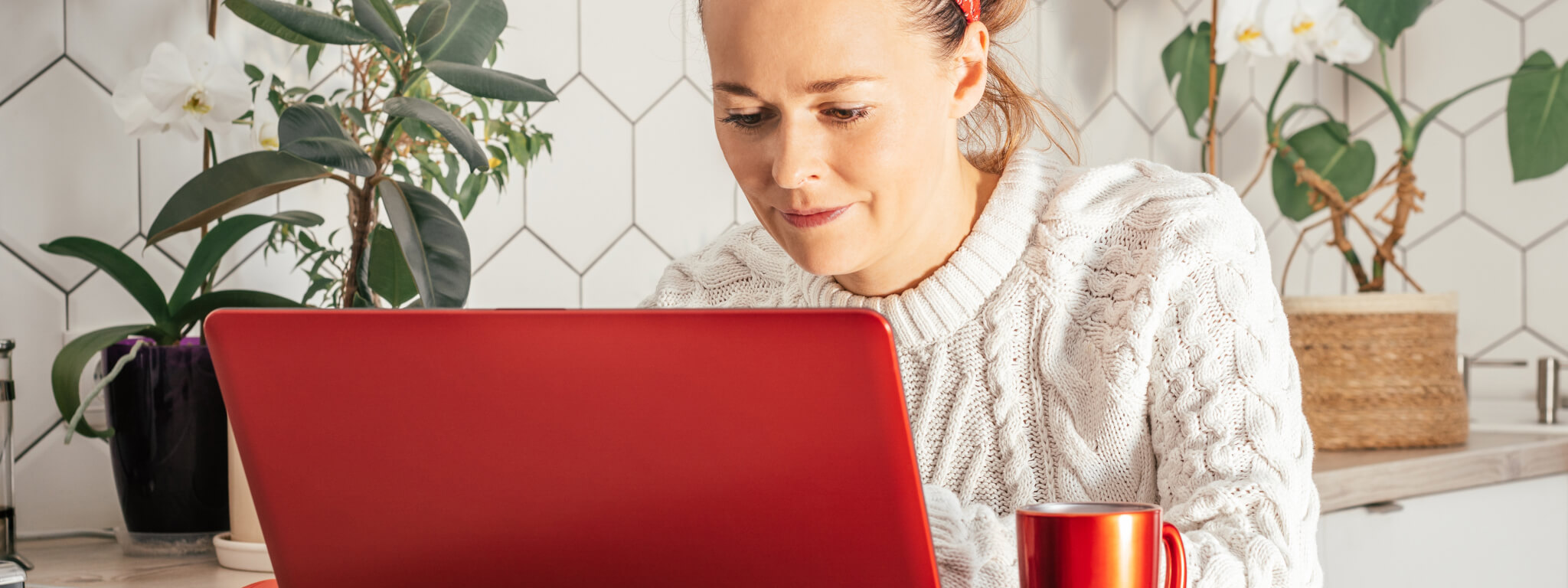 senhora em frente a um computador portátil vermelho com vasos de plantas à volta