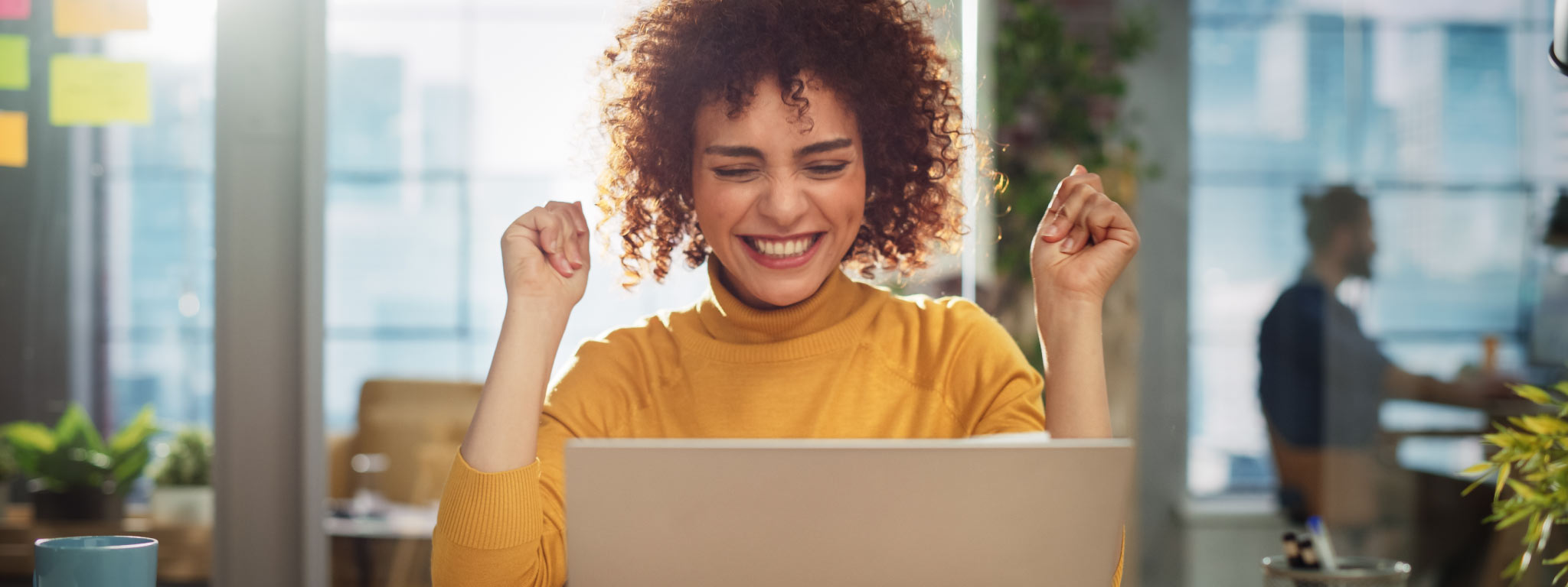  mulher sorri e festeja levantando os braços frente a laptop