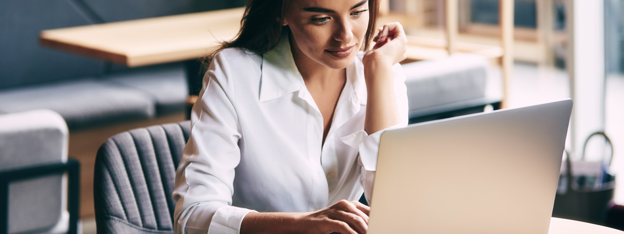 senhora de camisa branca sentada em frente a um computador portátil