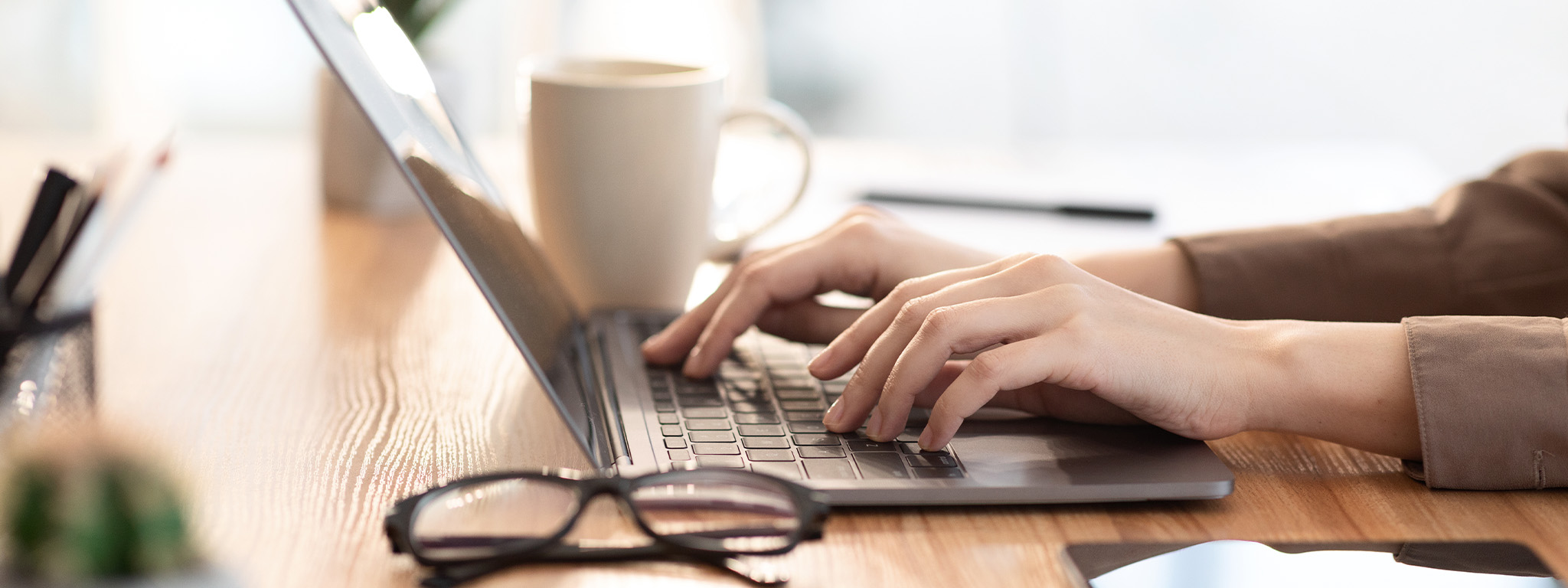 pessoa a trabalhar num computador com caneca e oculos ao lado