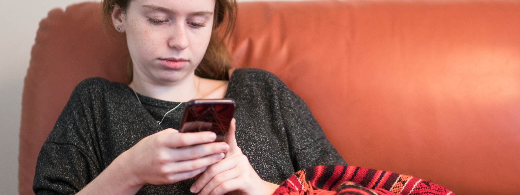 menina com telemóvel na mão sentada no sofá