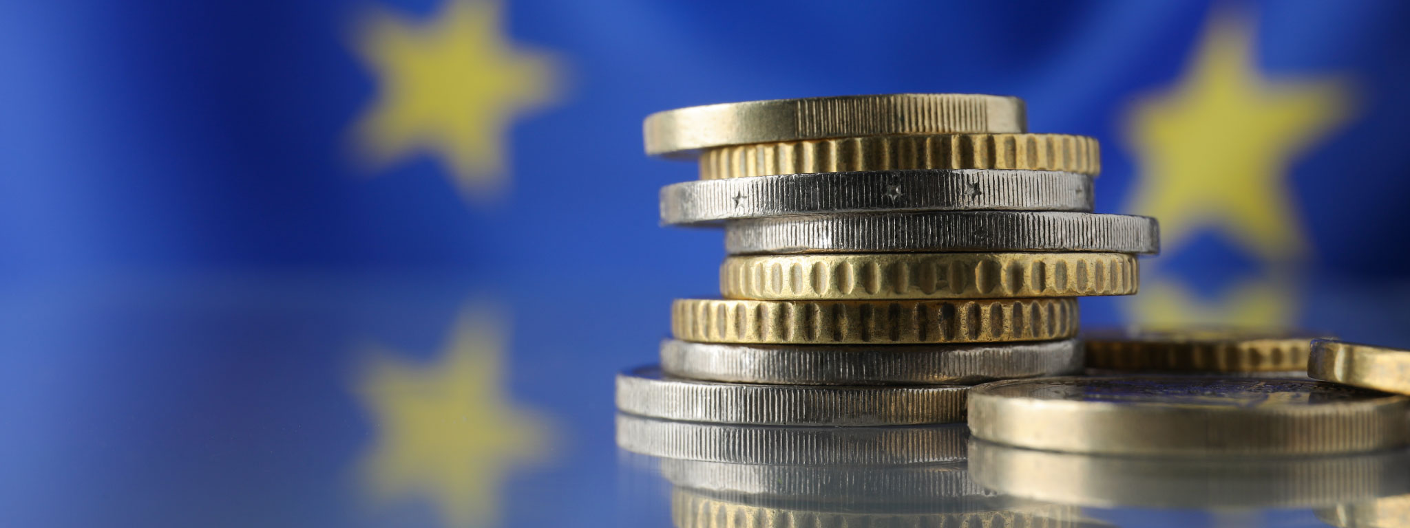  pilha de moedas em primeiro plano e bandeira de União Europeia como fundo