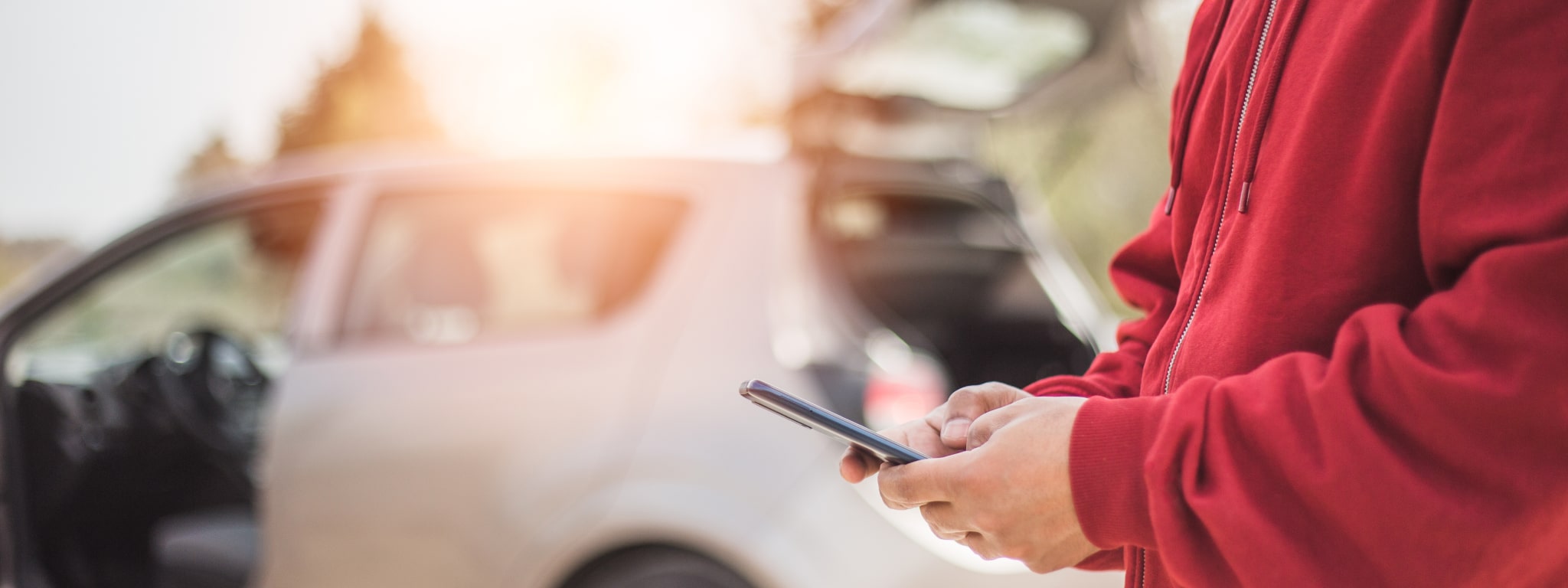 pessoa ao pé de um carro e com o telemóvel na mão