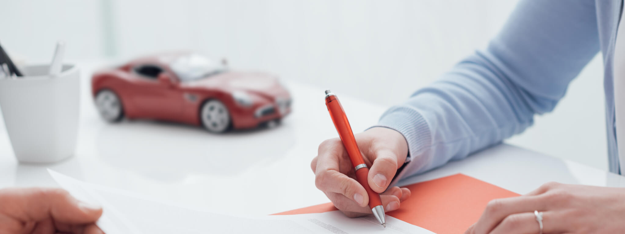 Pessoa a assinar um documento com um carro de brincar ao lado