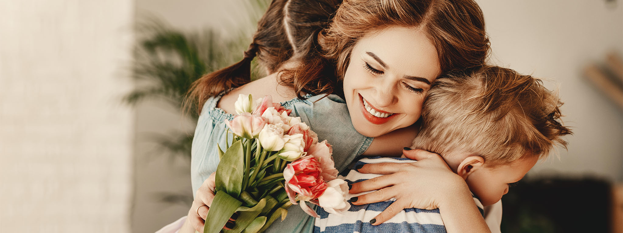 mãe a abraças os seus filhos com um ramo de flores na mão
