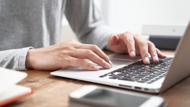 senhor em frente ao computador portátil com telemóvel ao lado