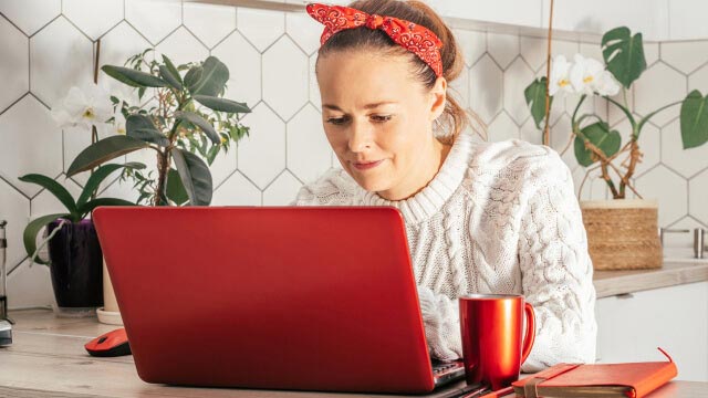 senhora ao computador portátil com caneca de chá ao lado e com ar satisfeito