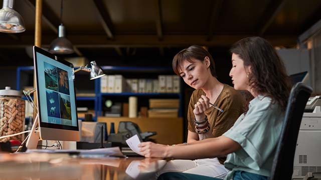 duas senhoras em frente a um computador e a falar em ambiente de trabalho