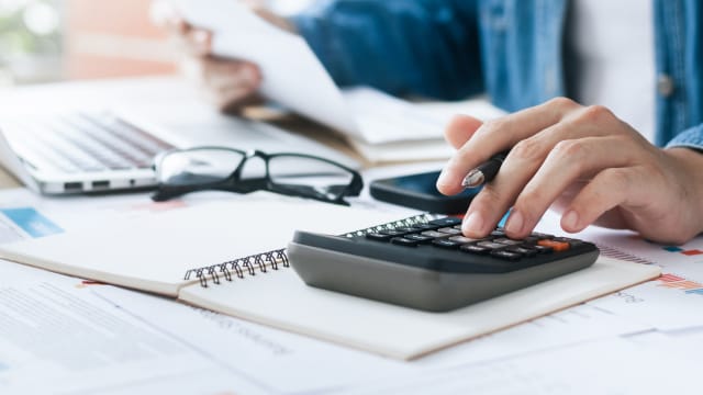 Senhor a fazer contas em calculadora sobre as deduções de prejuízos fiscais a fazer