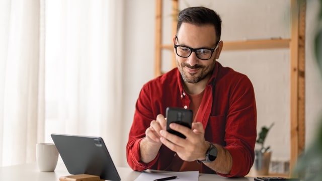 senhor com telemóvel na mão e com computador ao lado