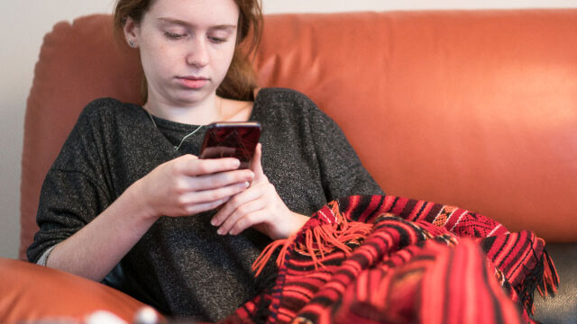 jovem com telemóvel na mão sentada no sofá