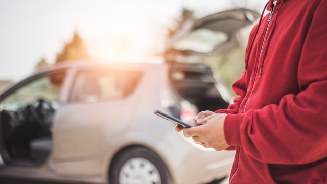 pessoa ao pé do carro com telemóvel na mão