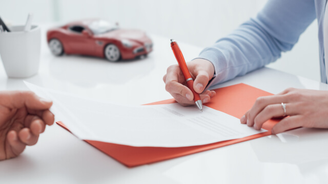 pessoa a assinar um documento com um carro vermelho de brincar ao lado