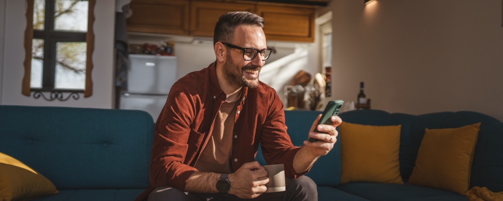 homem num sofá segura caneca e smartphone