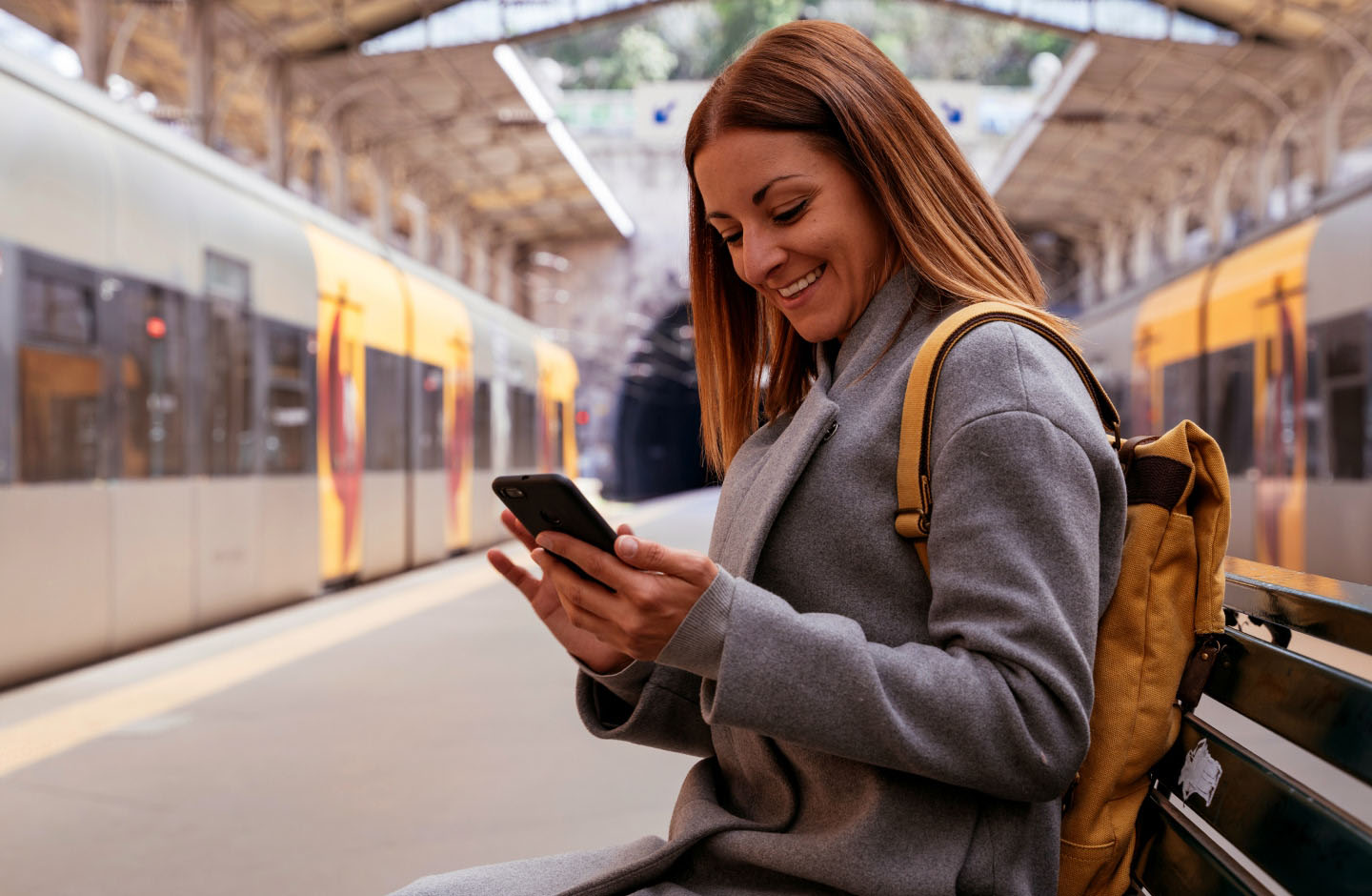 mulher sorridente a olhar para telemóvel em estação de comboios