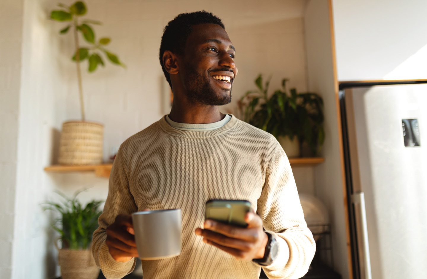 homem sorridente segura telemóvel e uma caneca