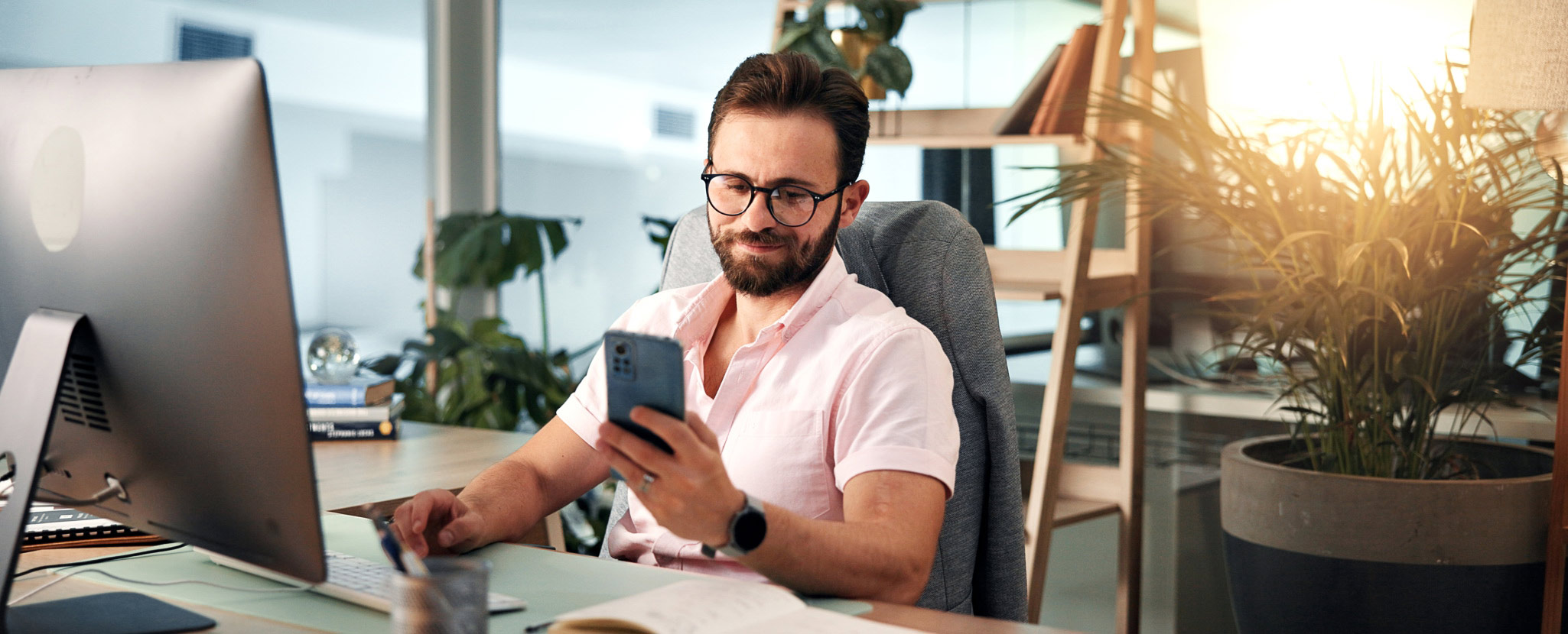 homem sentado à secretária a mexer em smartphone
