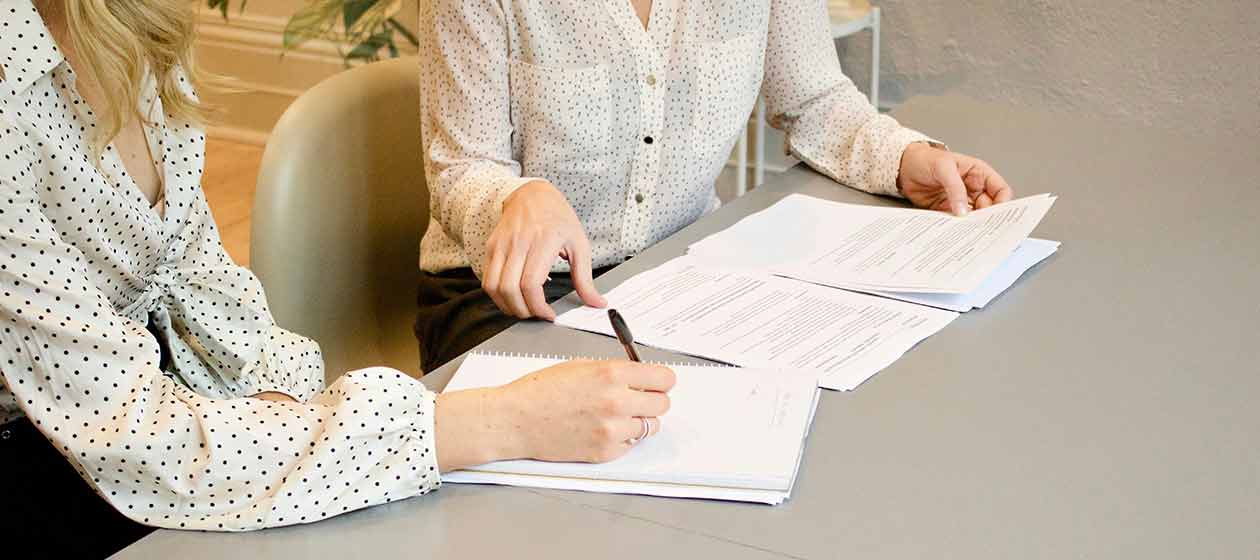 duas pessoas numa mesa a assinarem documentos impressos