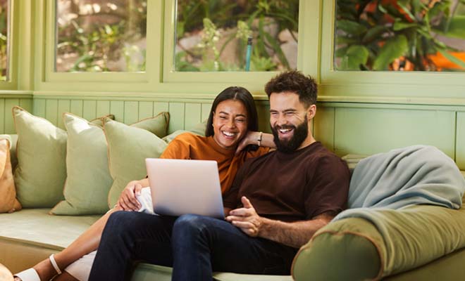 Casal feliz a simular crédito habitação no sofá.