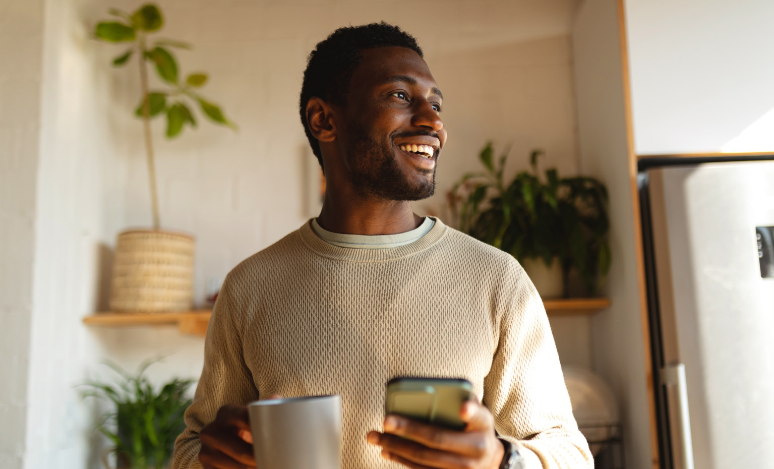 homem sorridente segura telemóvel e uma caneca
