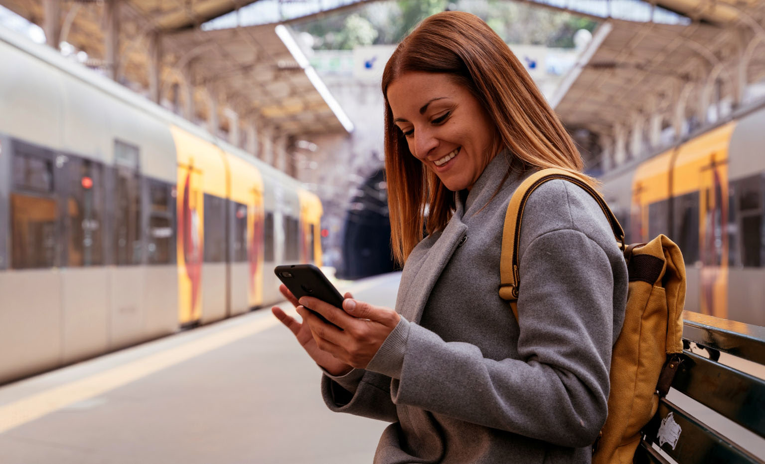 mulher sorridente a olhar para telemóvel em estação de comboios